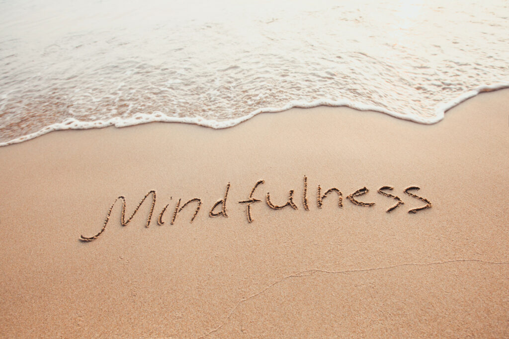 "mindfulness" written in the sand as the waves come in