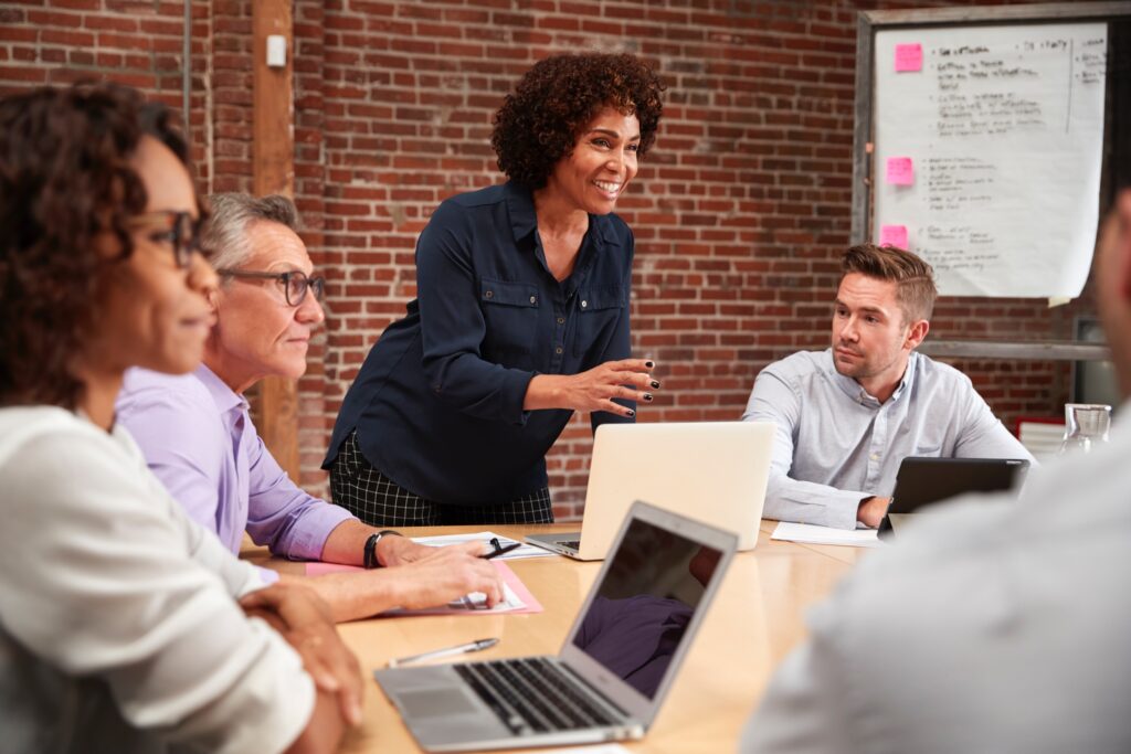 Mature businesswoman standing and leading diverse office meeting around table